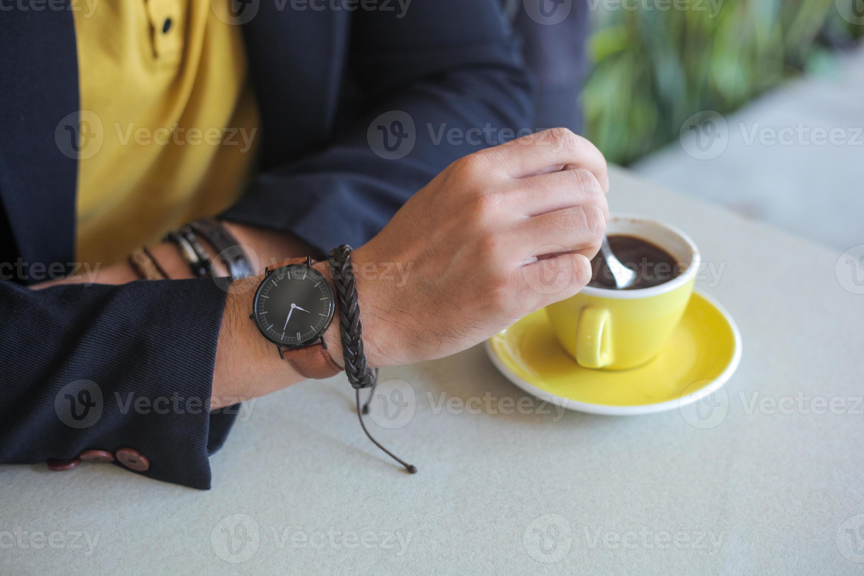 Hand of men wearing watches and bracelet stirring the coffee in a cup