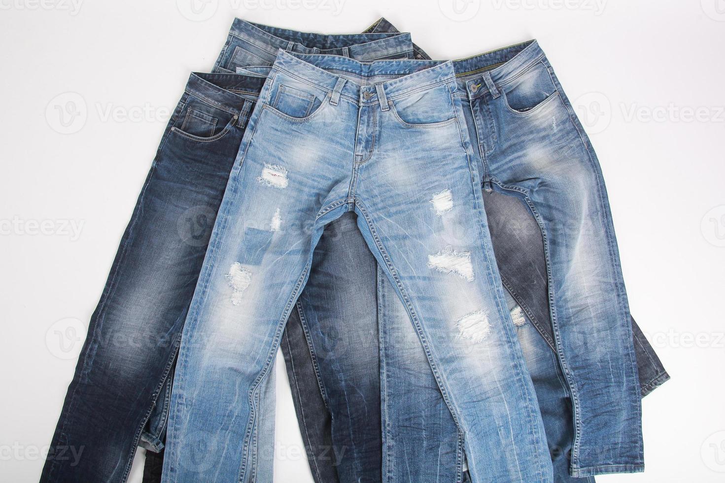 Various pile of denim pants on white background photo