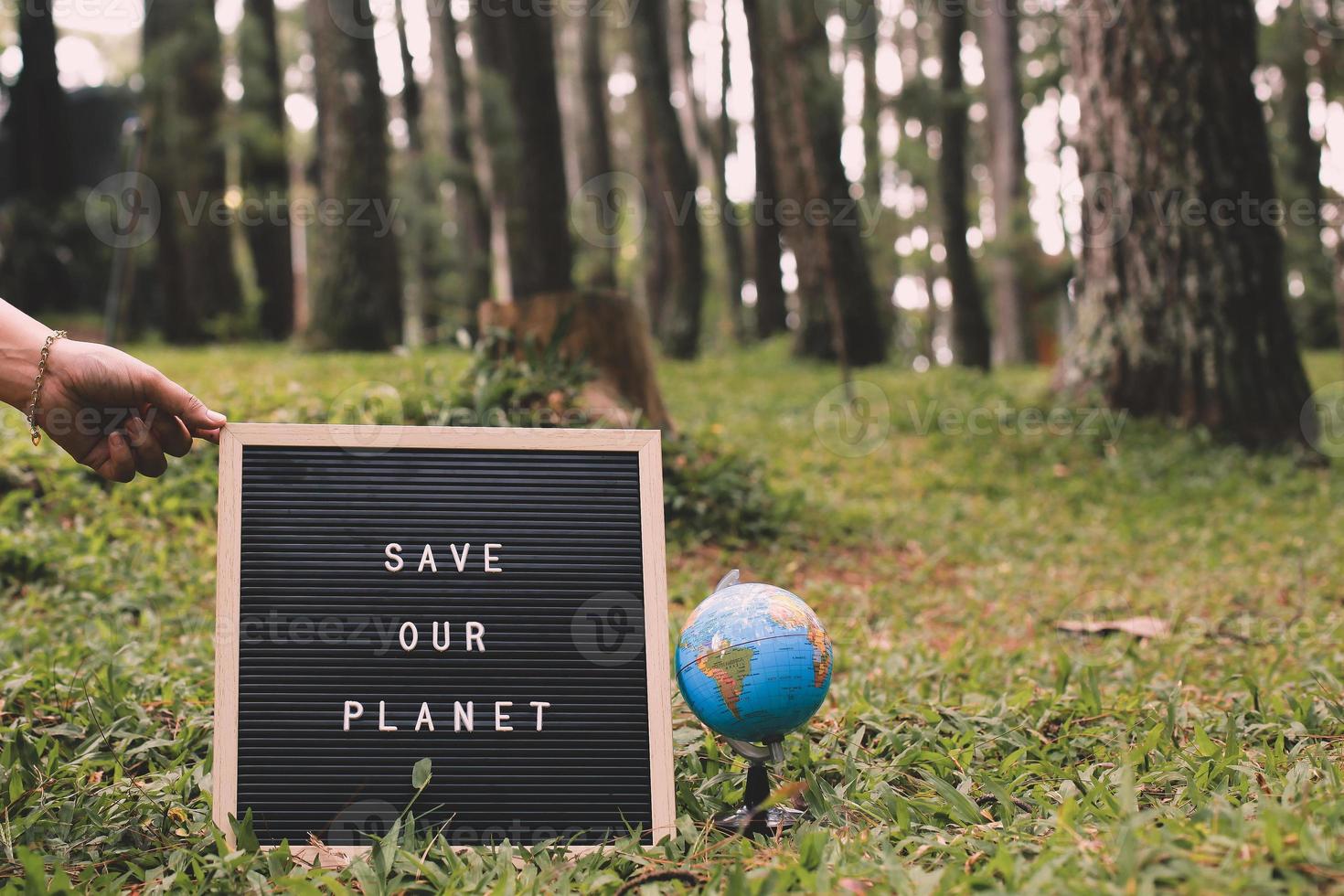 Quote on letter board says Save Our Planet with earth globe with forest background, earth day concept photo