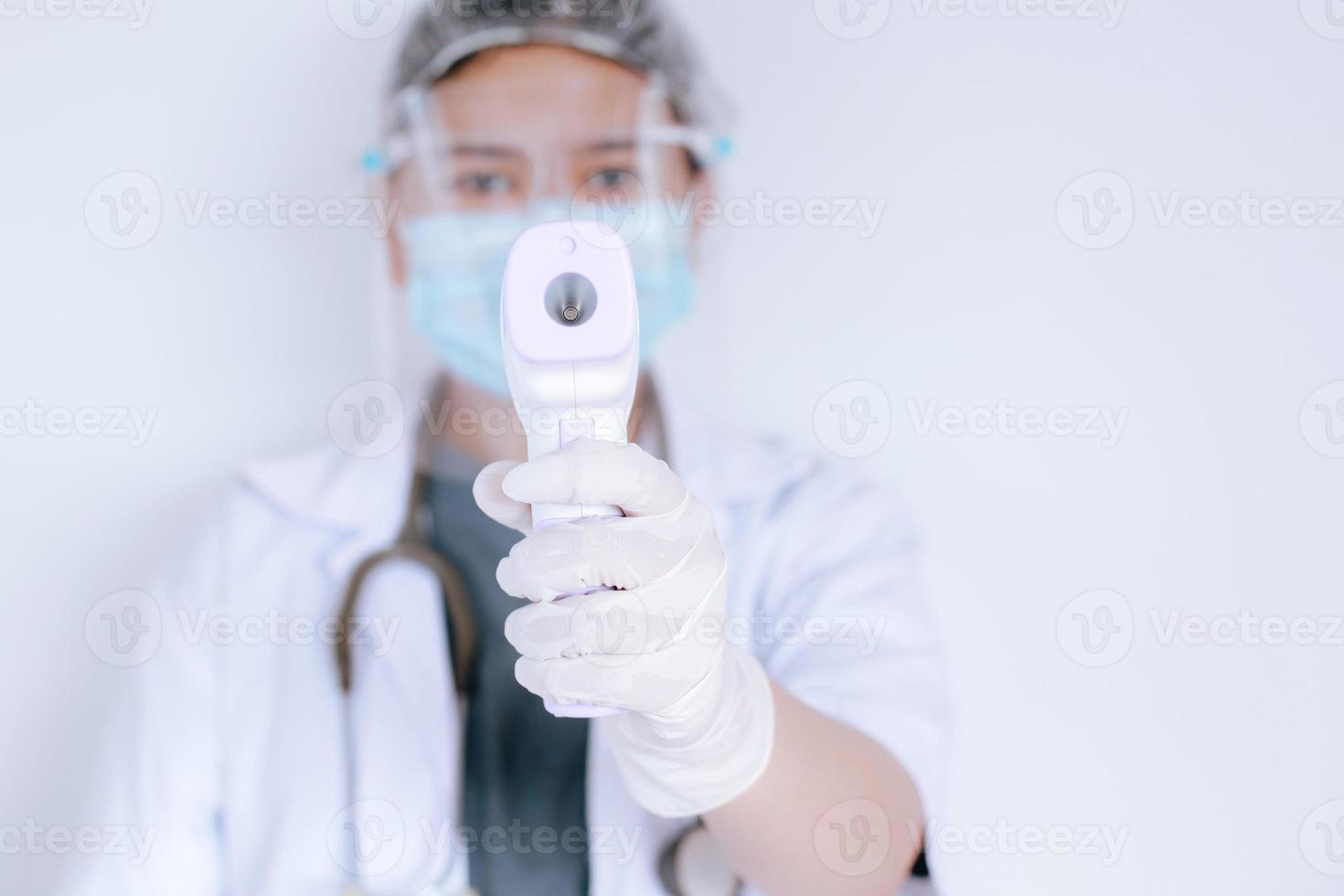 toma de primer plano de un médico que usa una máscara protectora lista para usar un termómetro de frente infrarrojo o una pistola de termómetro para verificar la temperatura corporal en busca de síntomas de virus y brotes de virus epidémicos foto