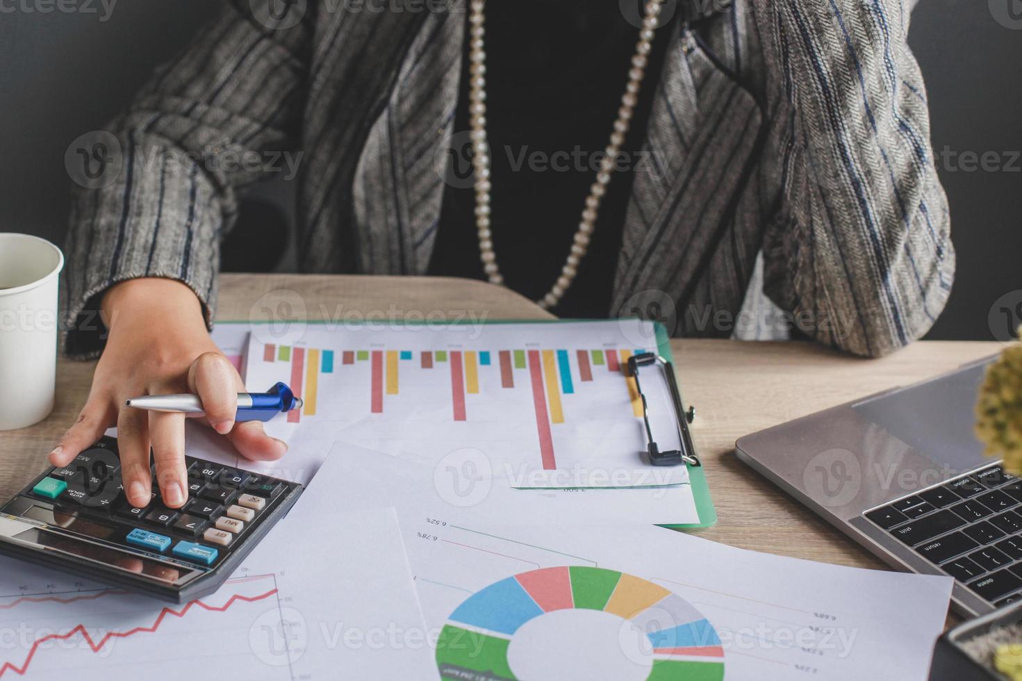 Cropped shot of business woman using  calculator with graph and chart on messy office desk. Financial report, business accounting, graph finance, analysis data charts photo