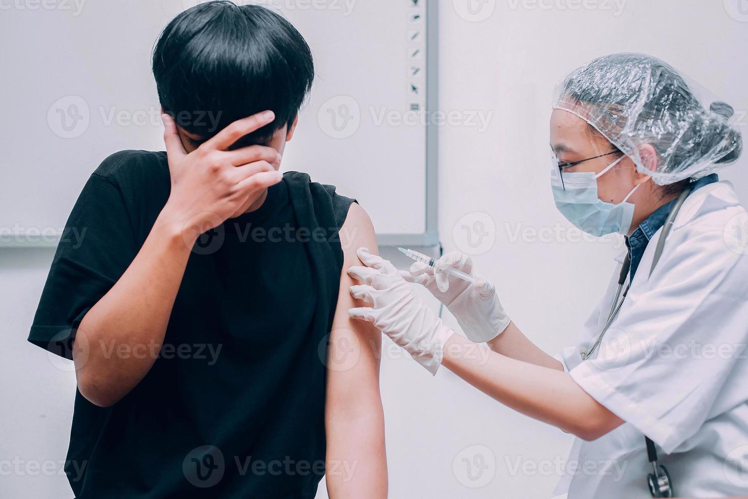 paciente joven con miedo o expresión de miedo que cubre su rostro cuando el médico le inyecta la vacuna foto