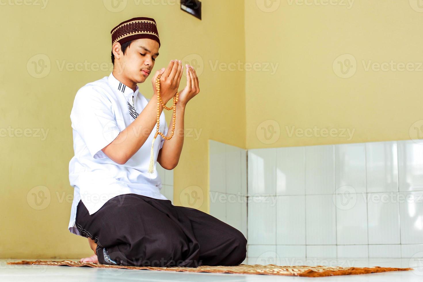 Portrait of young asian muslim praying to allah. Islam guy sitting with begging hand gesture and holding prayer beads in his hand photo