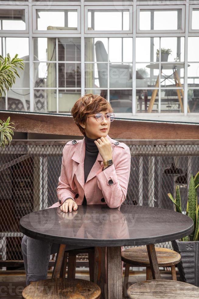 Fashionable woman in glasses and pink coat sitting on the chair in coffee shop photo