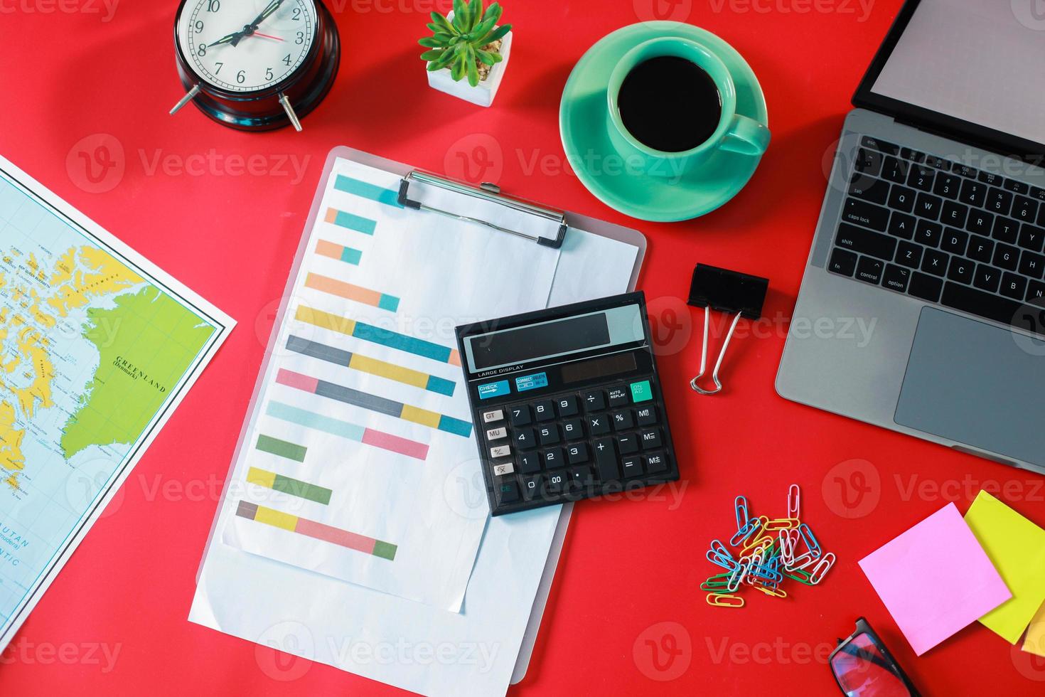 vista superior plana de una oficina elegante con una computadora portátil, una suculenta, una taza de café y accesorios de oficina desordenados aislados en un fondo rojo foto