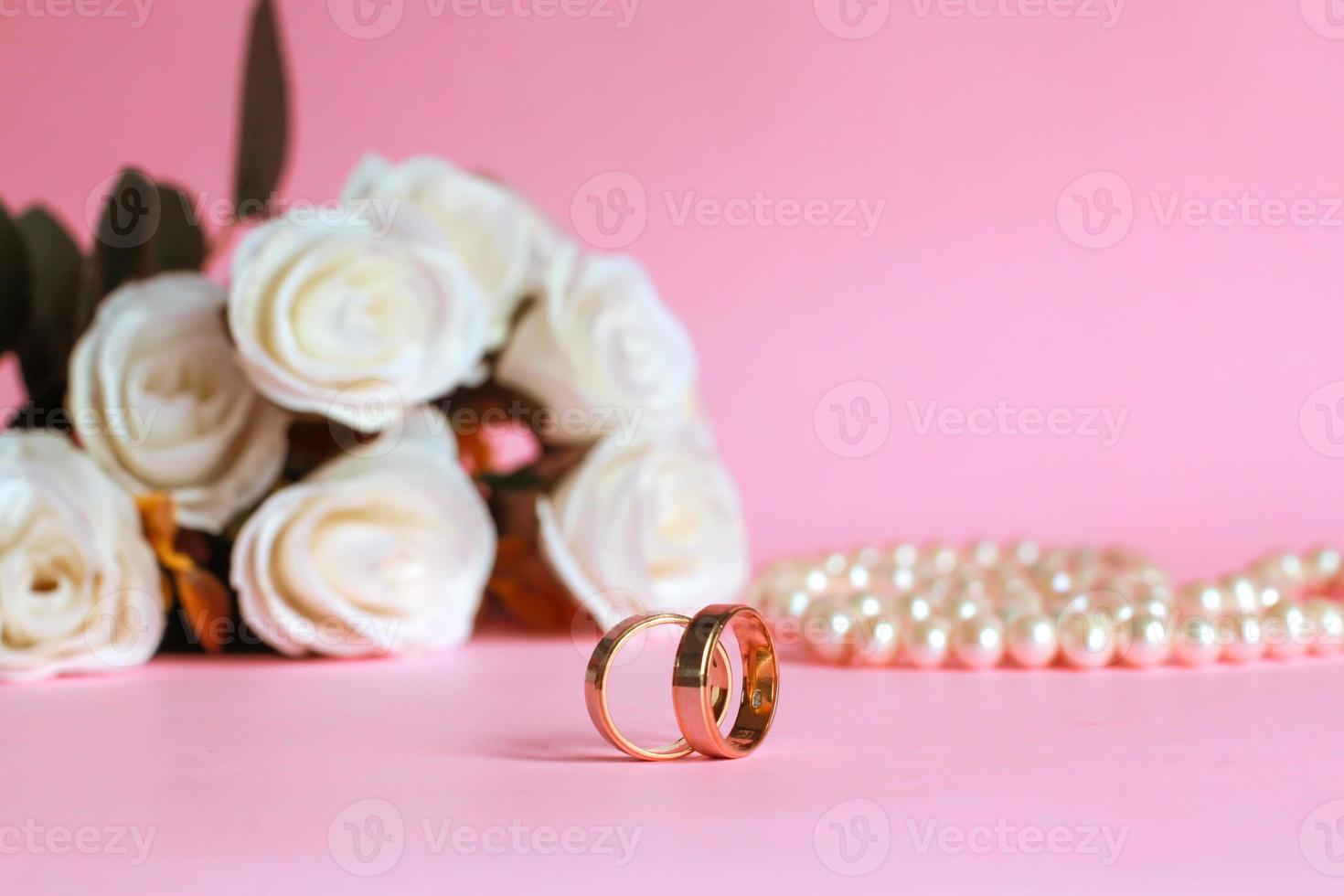 anillo de boda con rosa blanca borrosa y collar de perlas en el fondo aislado en rosa foto