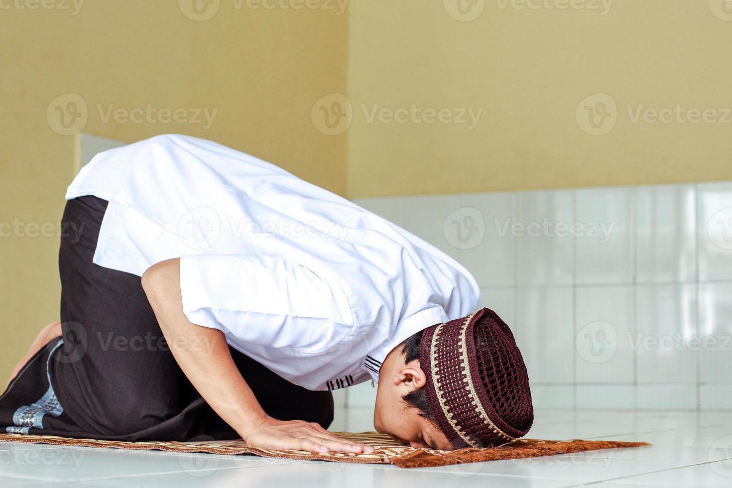 Side view of asian muslim man doing Salat with prostration pose on the prayer mat photo