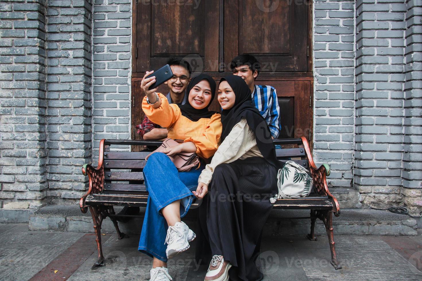 Four young friends sitting outdoors. Group of people sitting while selfie using smart phone photo