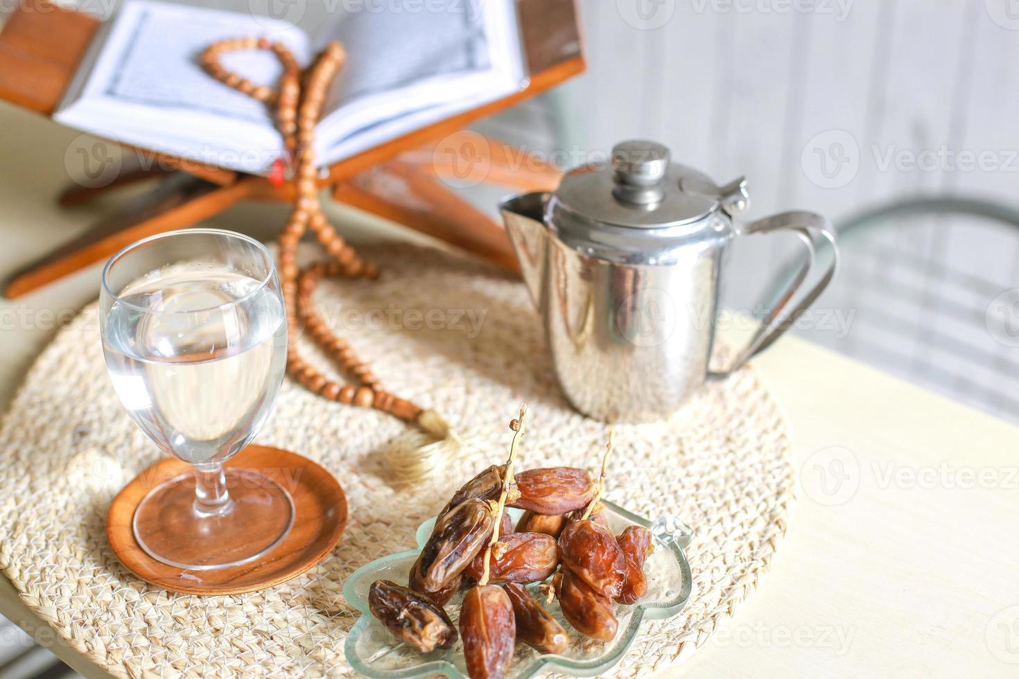 vista superior de kurma o dátiles con vaso de agua, libro sagrado al-quran, tetera y cuentas de oración sobre la mesa. Ramadán tradicional, comida iftar. concepto de mes de ayuno ramadan kareem foto