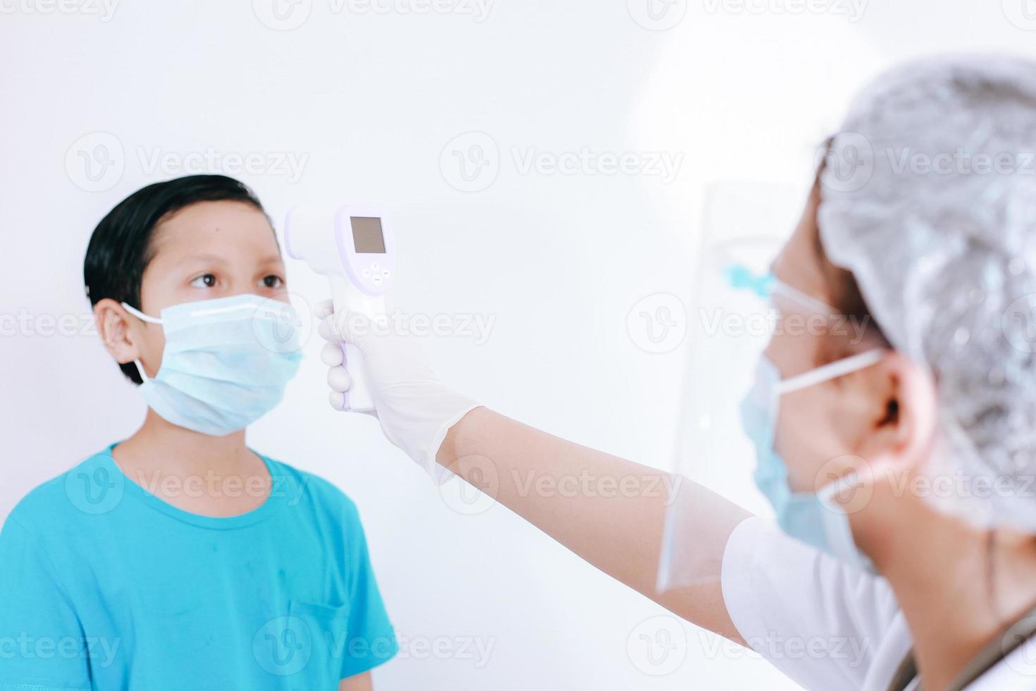 Nurse or doctor checks boy body temperature using infrared forehead thermometer gun for virus symptom photo
