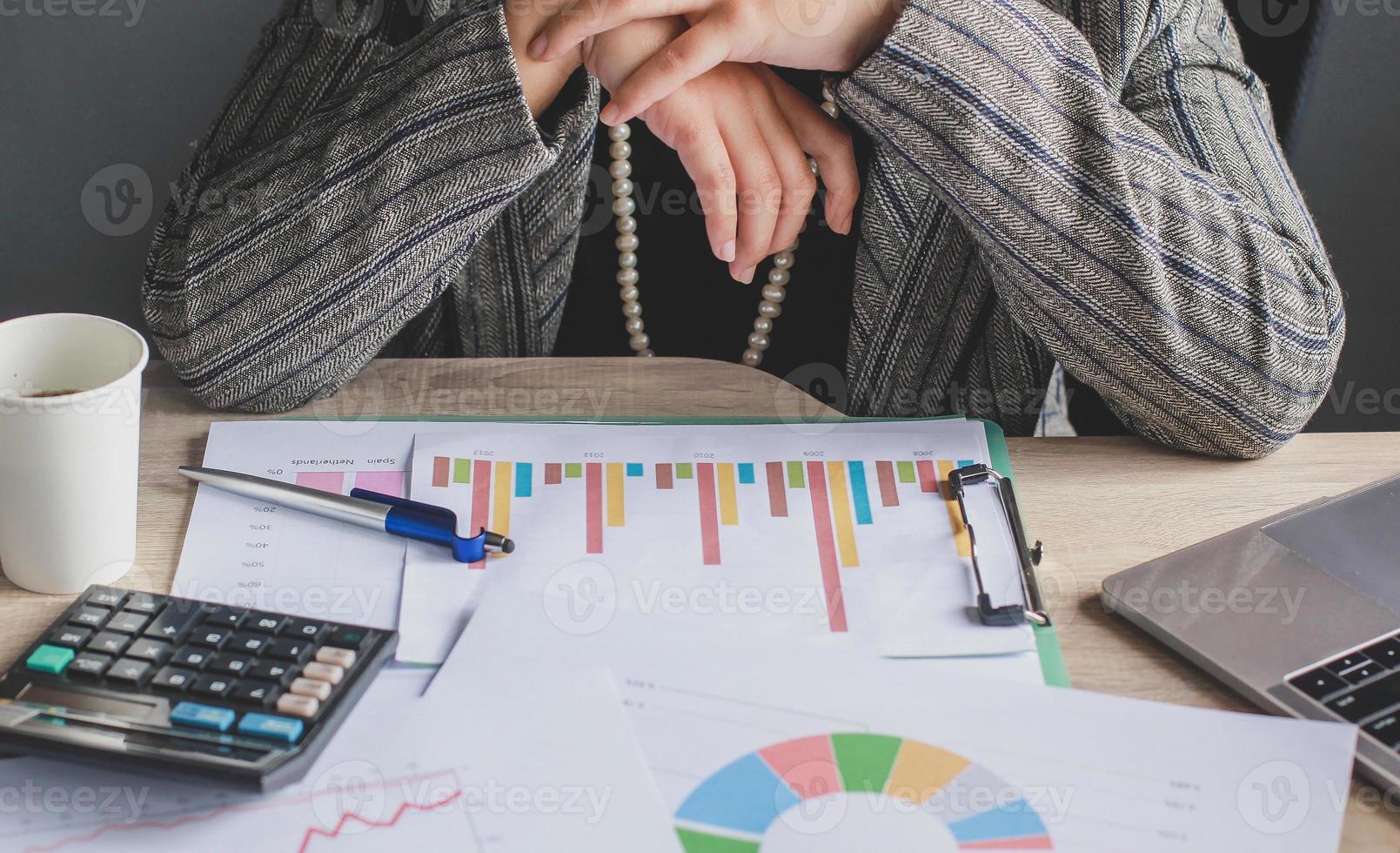 Cropped shot of business woman is sitting while reading graph and chart on clip board with messy office desk photo