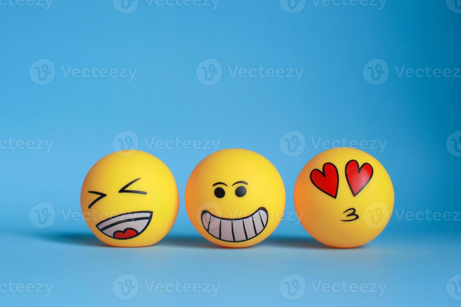 Laugh emoticon, smiley emoticon and love on face emoticon with mouth kissing isolated on blue background. photo