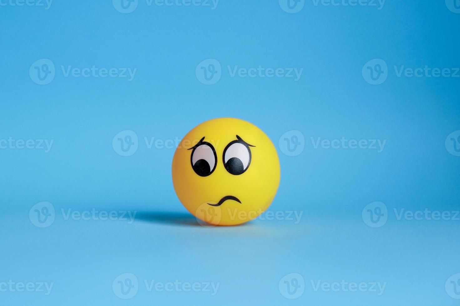 Thinking yellow face with furrowed eyebrows or confused emoticon isolated on blue background photo