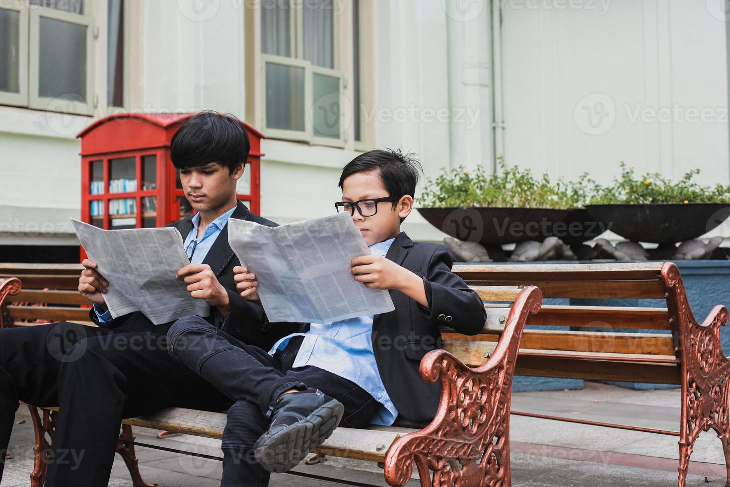 Two teenager with black suit sitting on the chair while reading newspaper photo