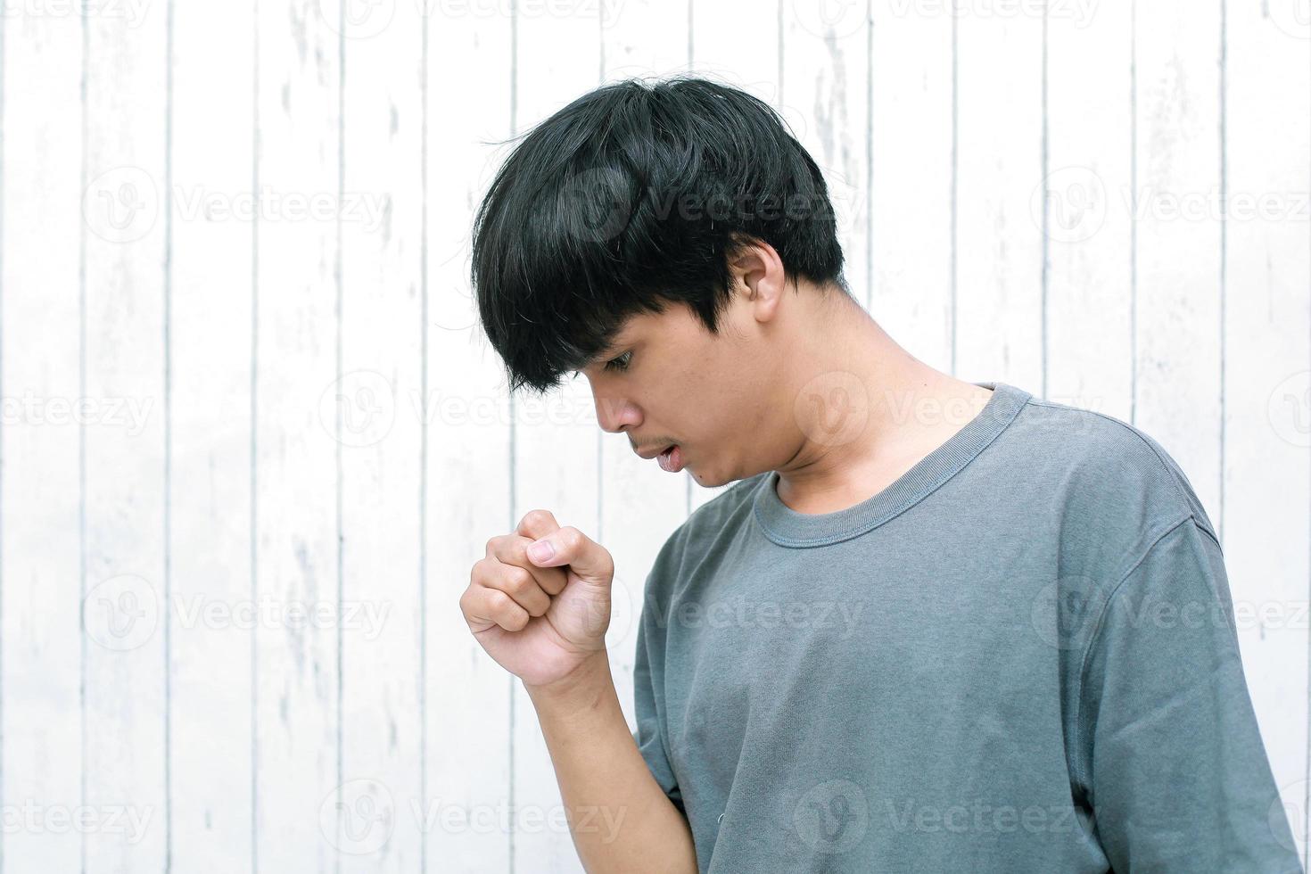 Asian young man feeling unwell and coughing as symptom for cold or bronchitis photo