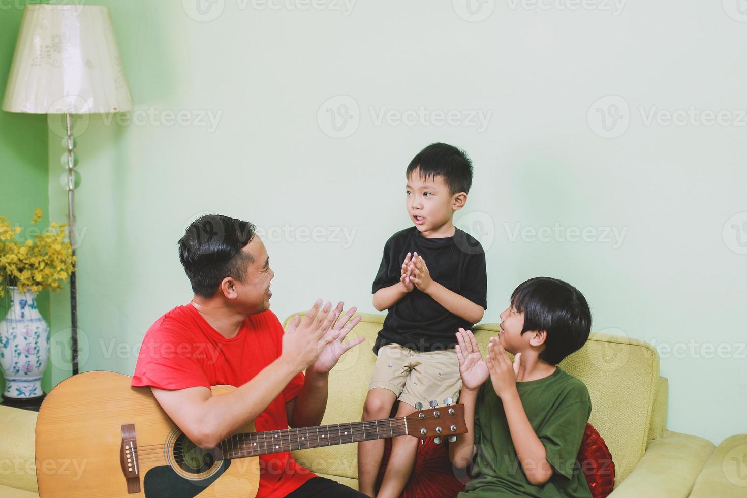 Happy asian father singing and clapping hand together with his son at home photo