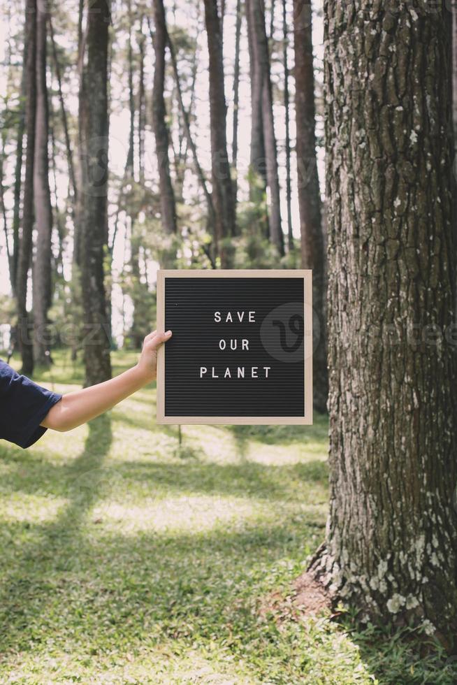 Hand holding a letter board that says save our planet on the forest, earth day concept. photo