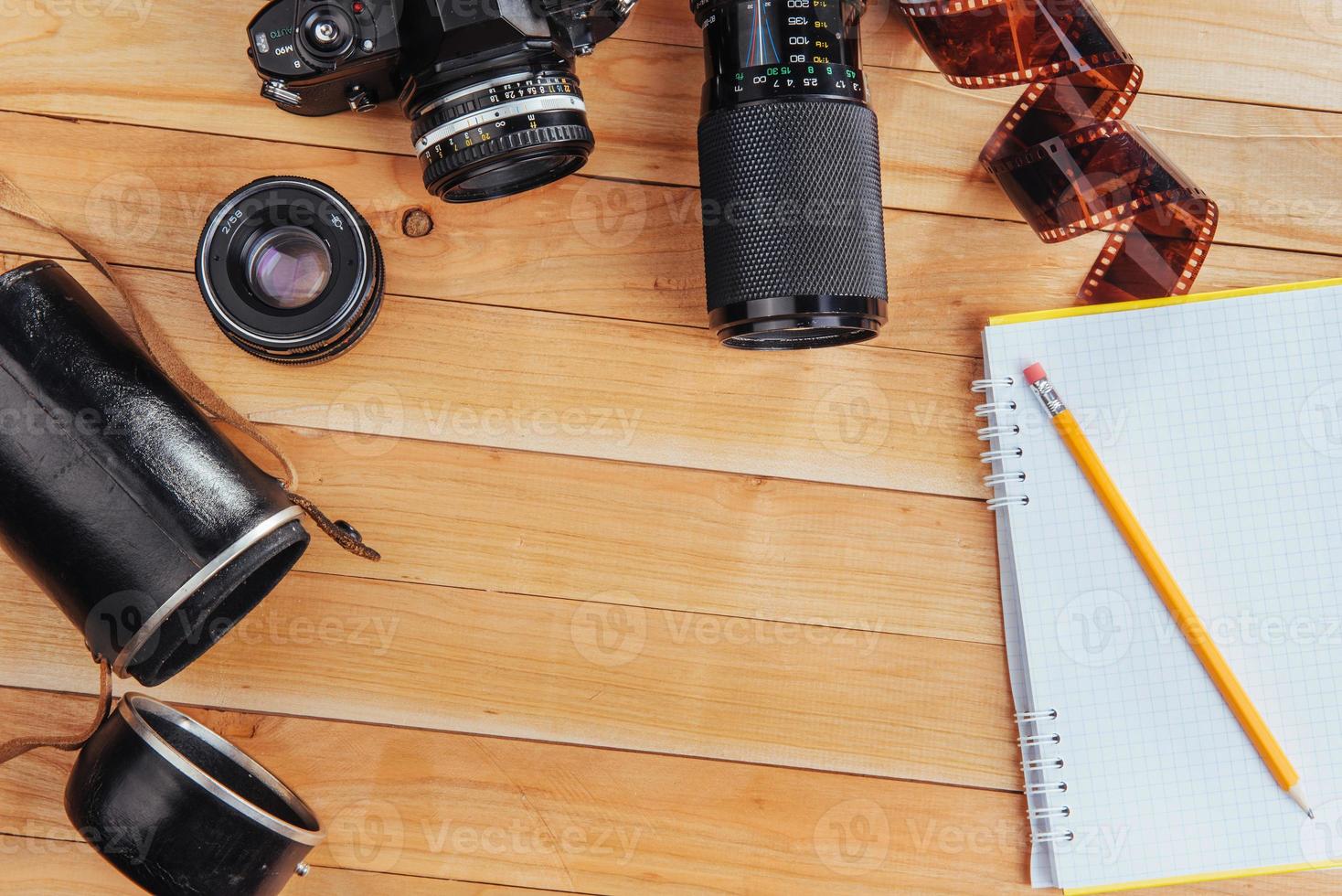 The old film camera and roll film and notebook with pencil on a wooden background photo