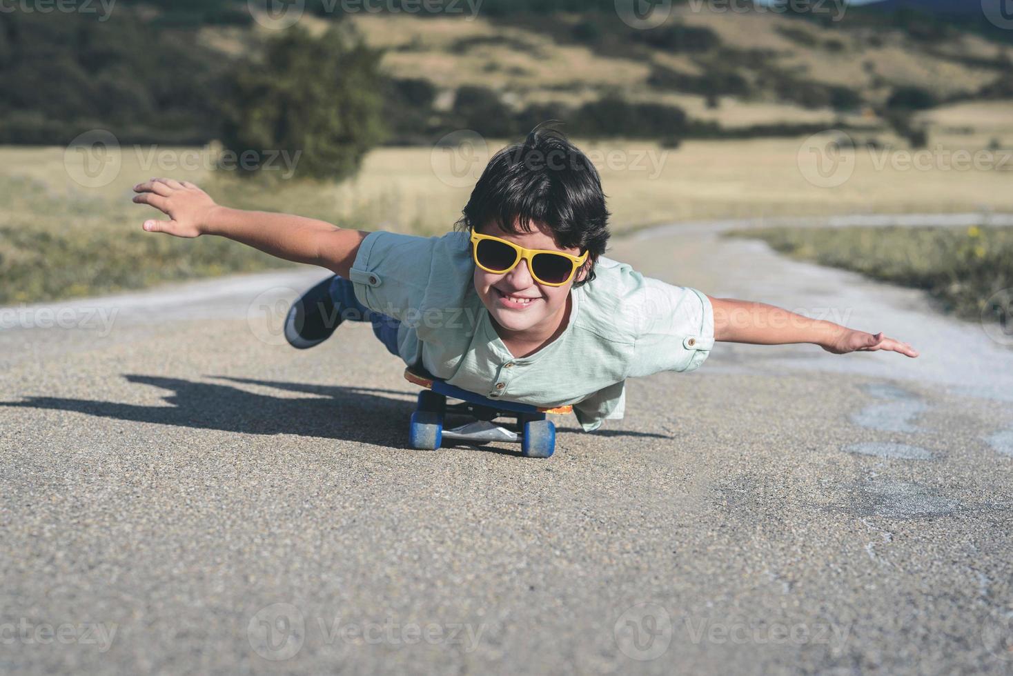 niño feliz con monopatín y gafas de sol en la carretera foto