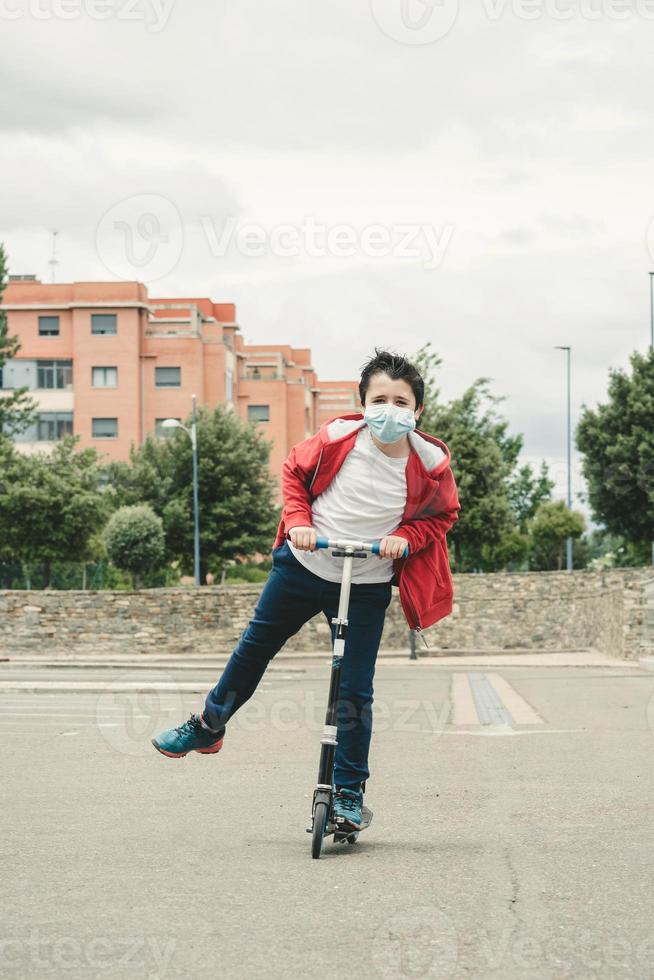 happy kid wearing medical mask with his scooter in the city photo