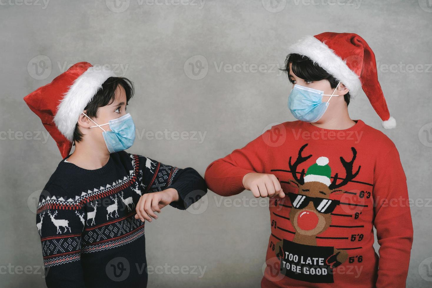 feliz navidad, dos niños con máscara médica y sombrero de santa claus golpean los codos, concepto de distanciamiento social foto