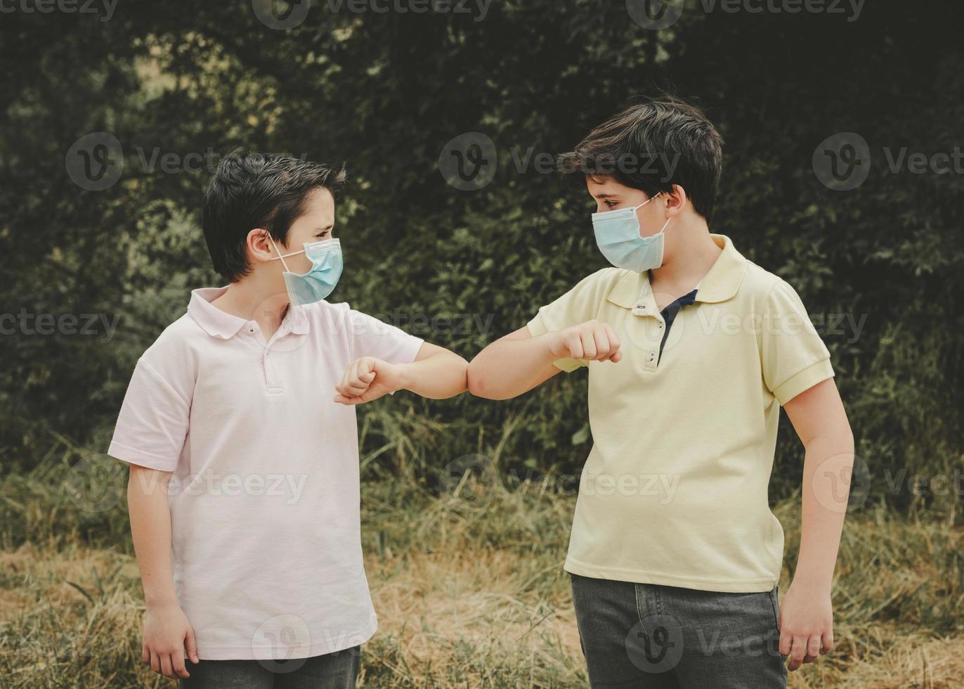 two kids with medical mask bump elbows, social distancing concept photo