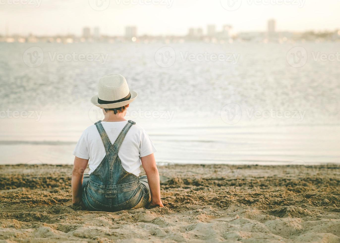Back view of a Pensive child sitting on the beach outdoor photo