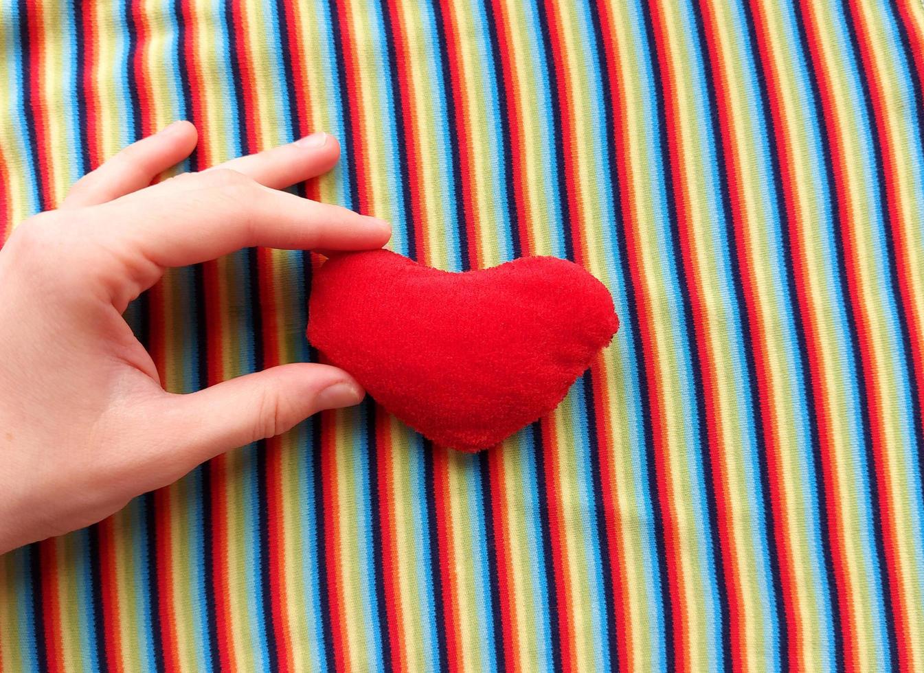 red heart in hand on a background of rainbow fabric. place for text. bright banner, concept. love. copy space. photo