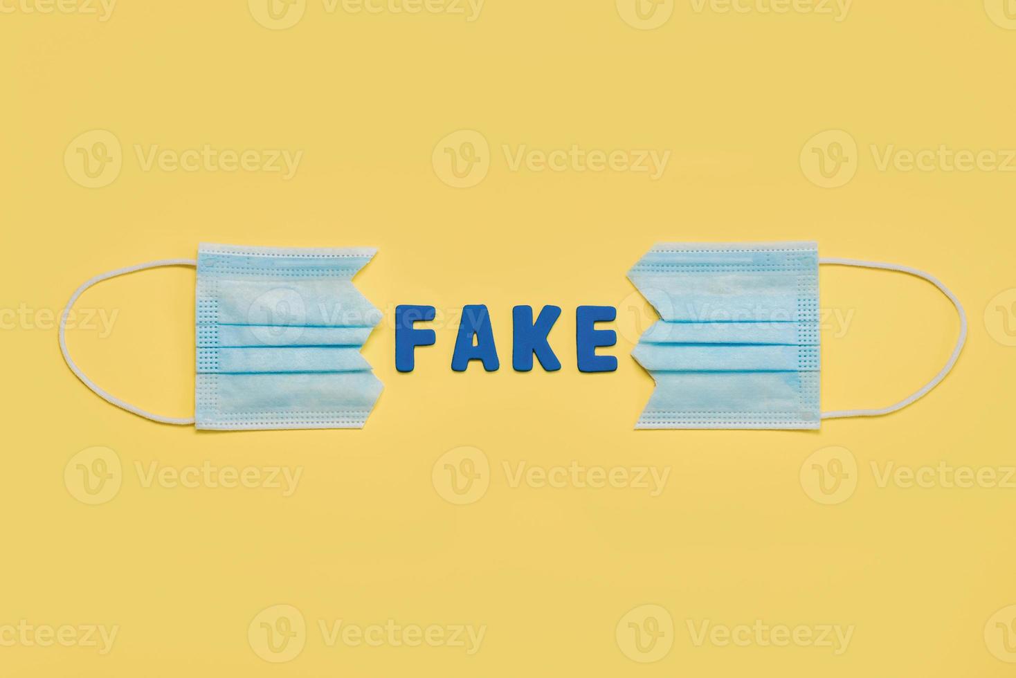 Protective surgical mask split in two with letters forming the word fake.Concept of protesting against coronavirus scams photo