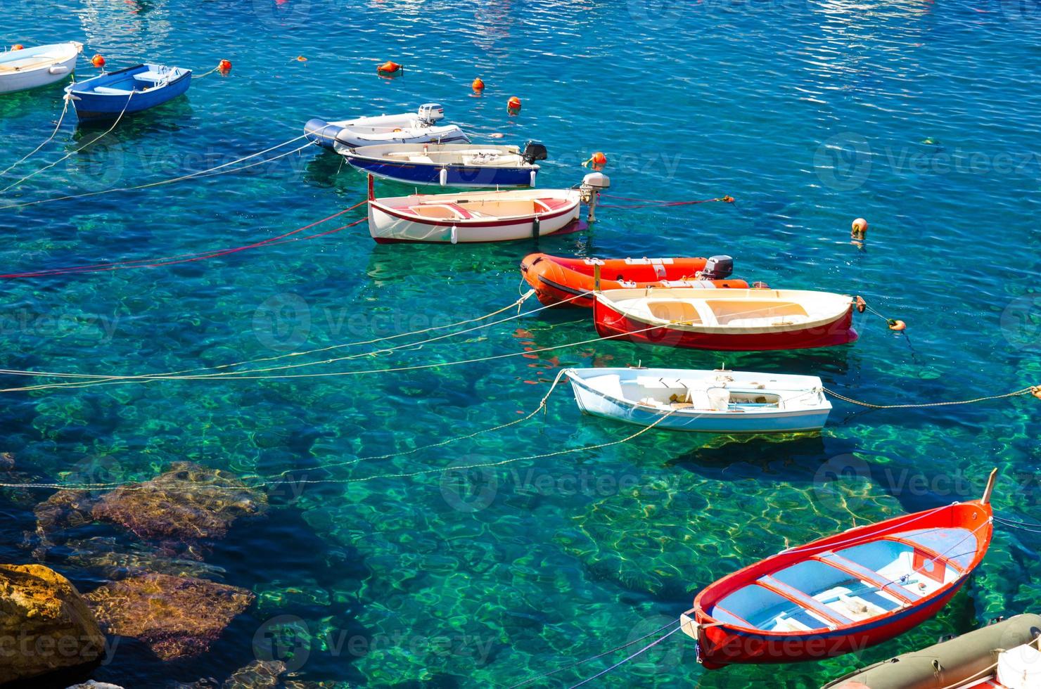 Fishing colorful multicolored boats on transparent clear water with visible bottom in small stone harbor of Riomaggiore village National park Cinque Terre coast, Ligurian and Mediterranean Sea, Italy photo