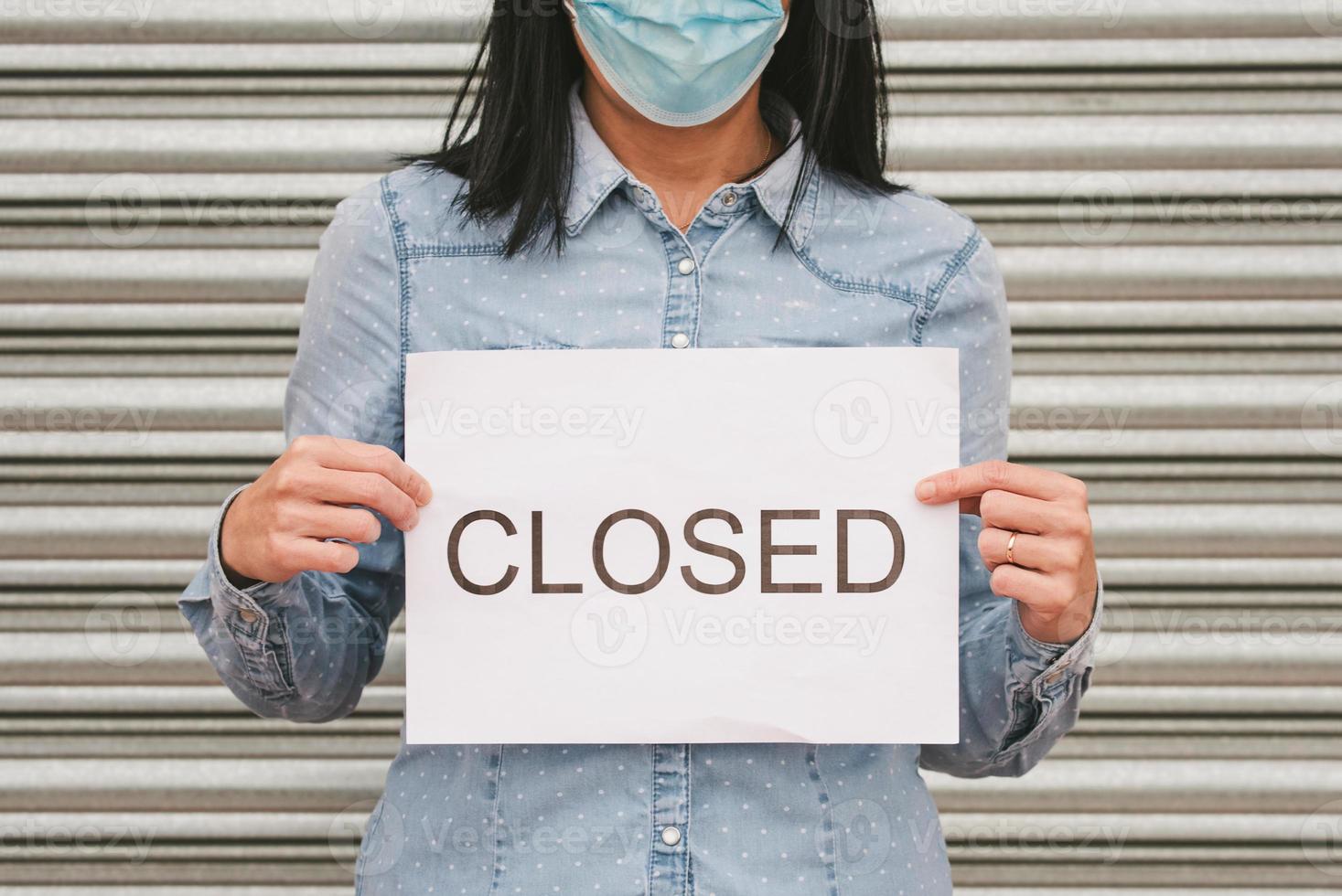 coronavirus.mujer con mascarilla médica sosteniendo un cartón blanco con el texto cerrado foto
