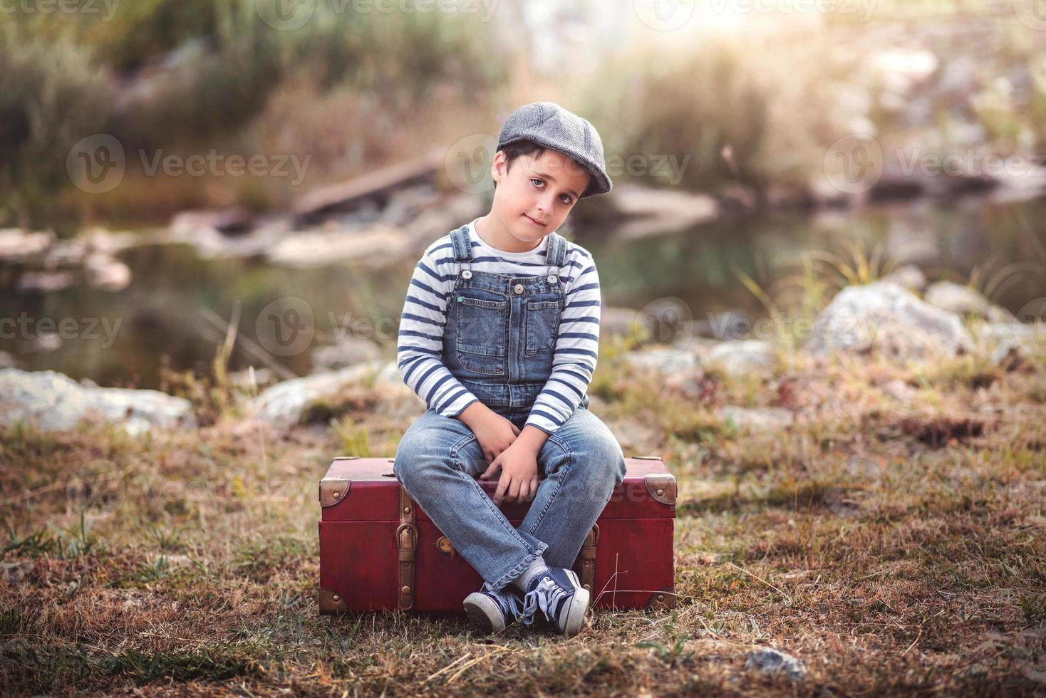 niño pensativo sentado en una maleta foto