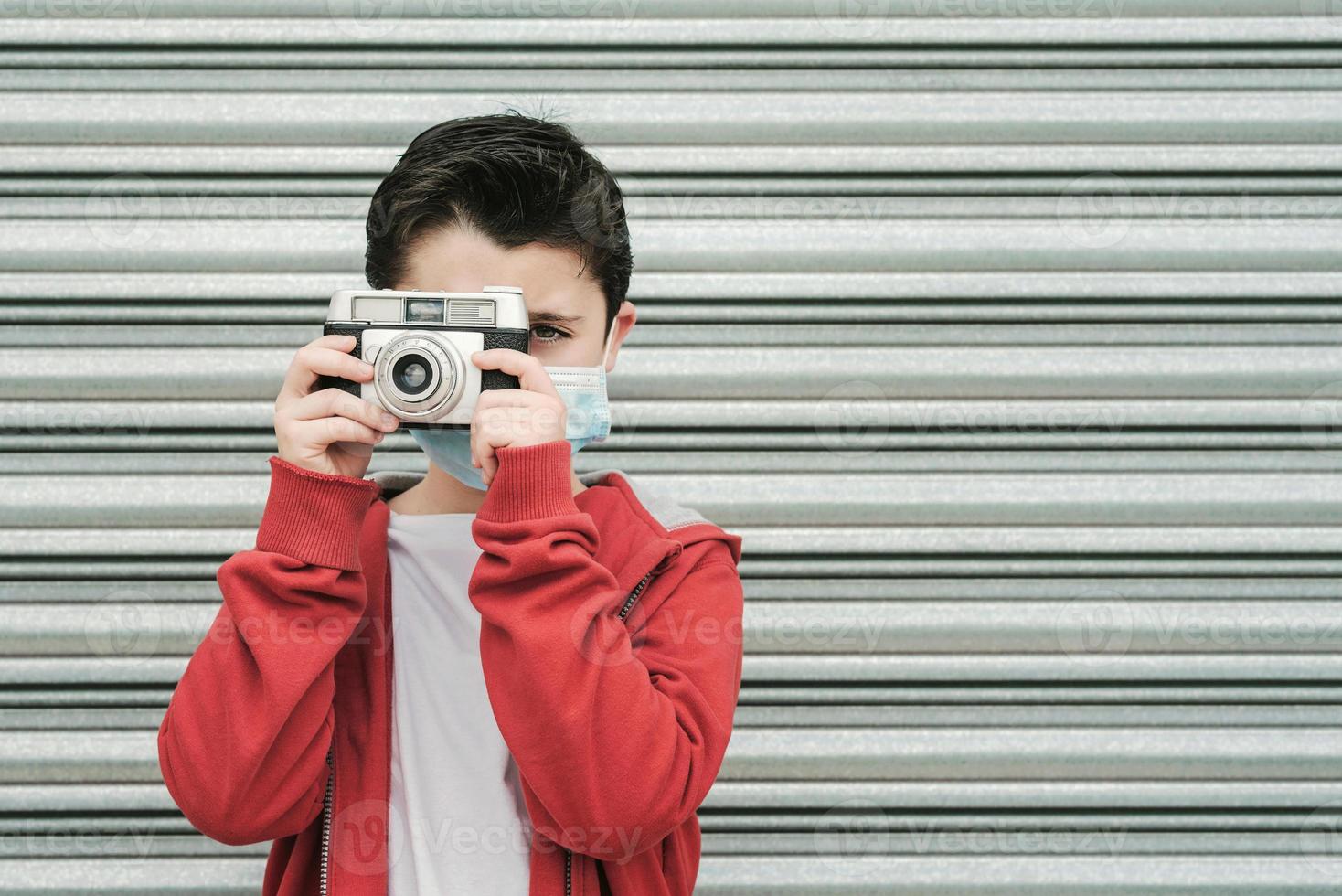 niño con máscara médica toma fotos con su cámara