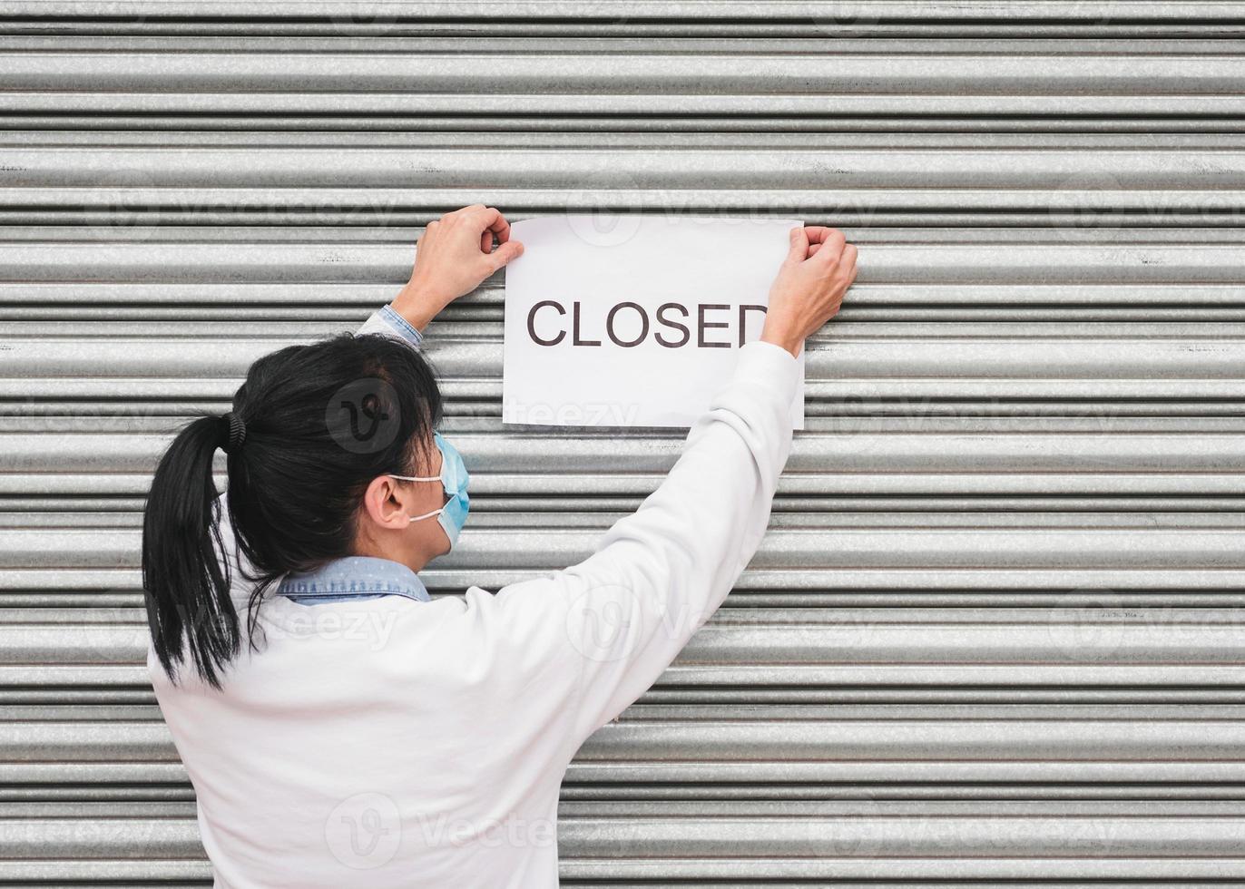 Coronavirus.Woman with medical face mask hangs information about the your store closing photo