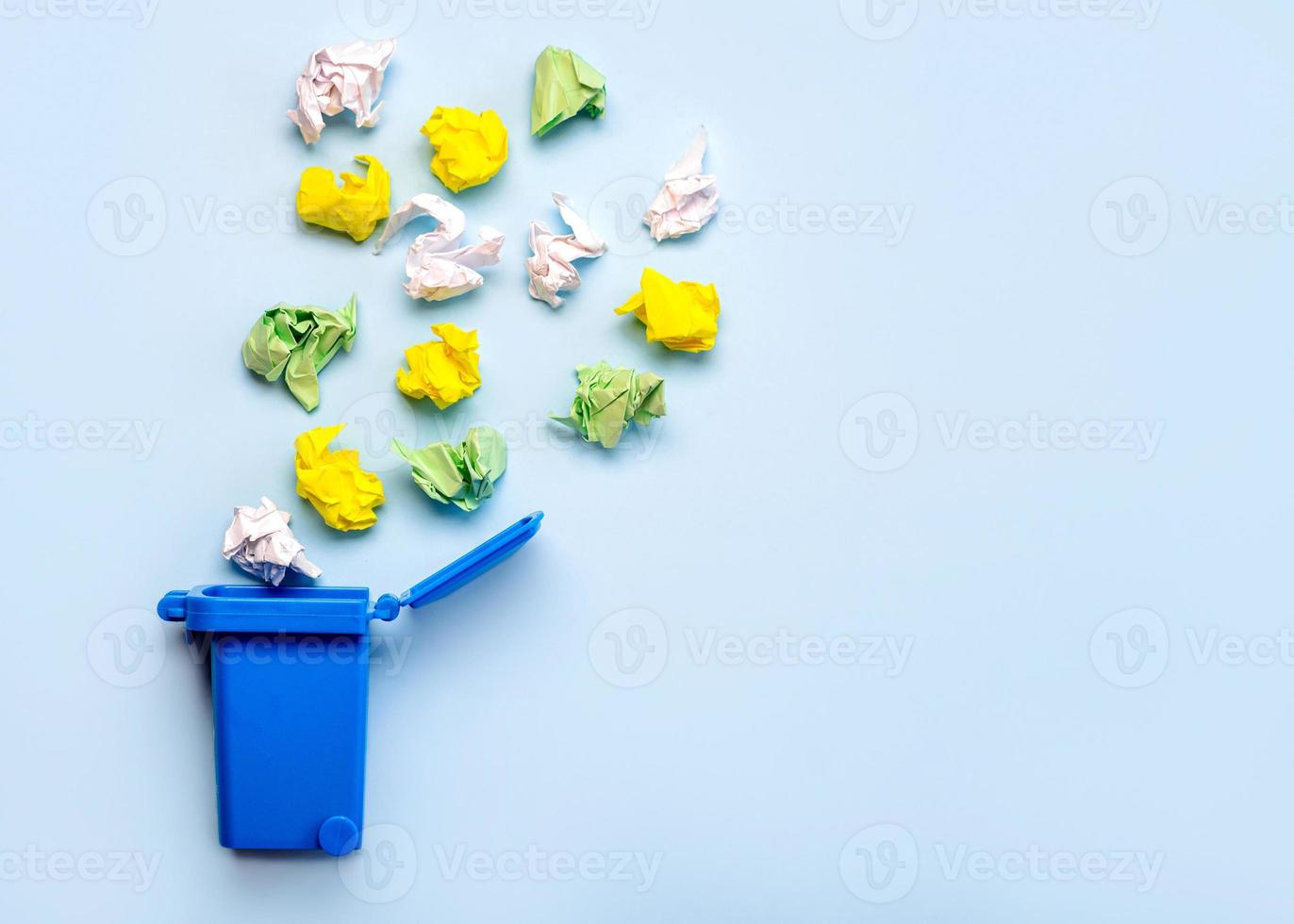 Blue recycle bin with crumpled colored paper balls with copy space.Paper recycling concept photo