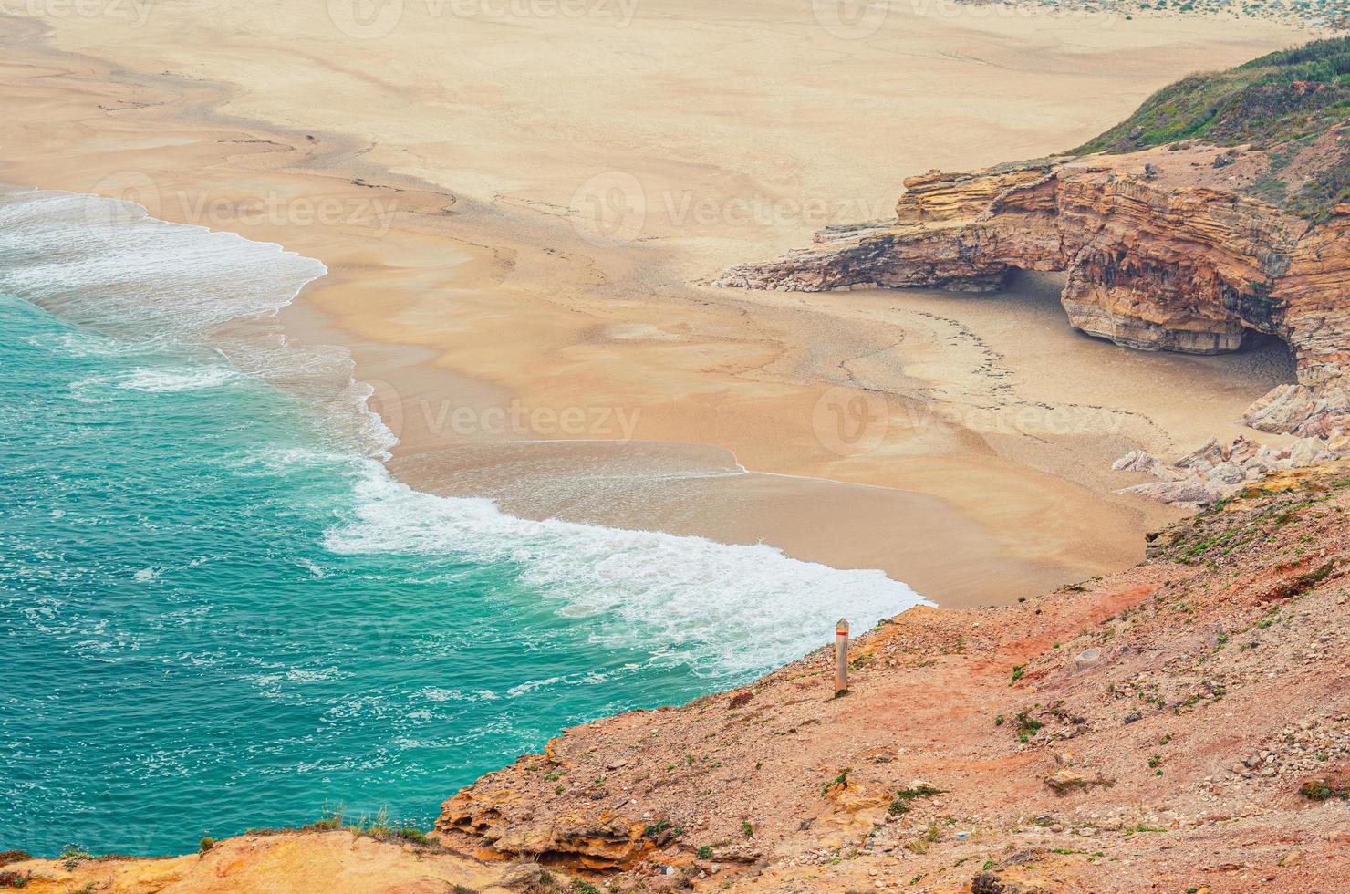 Top aerial view of sandy beach with rocks and cliffs and waves of azure turquoise water of Atlantic Ocean near Nazare town photo