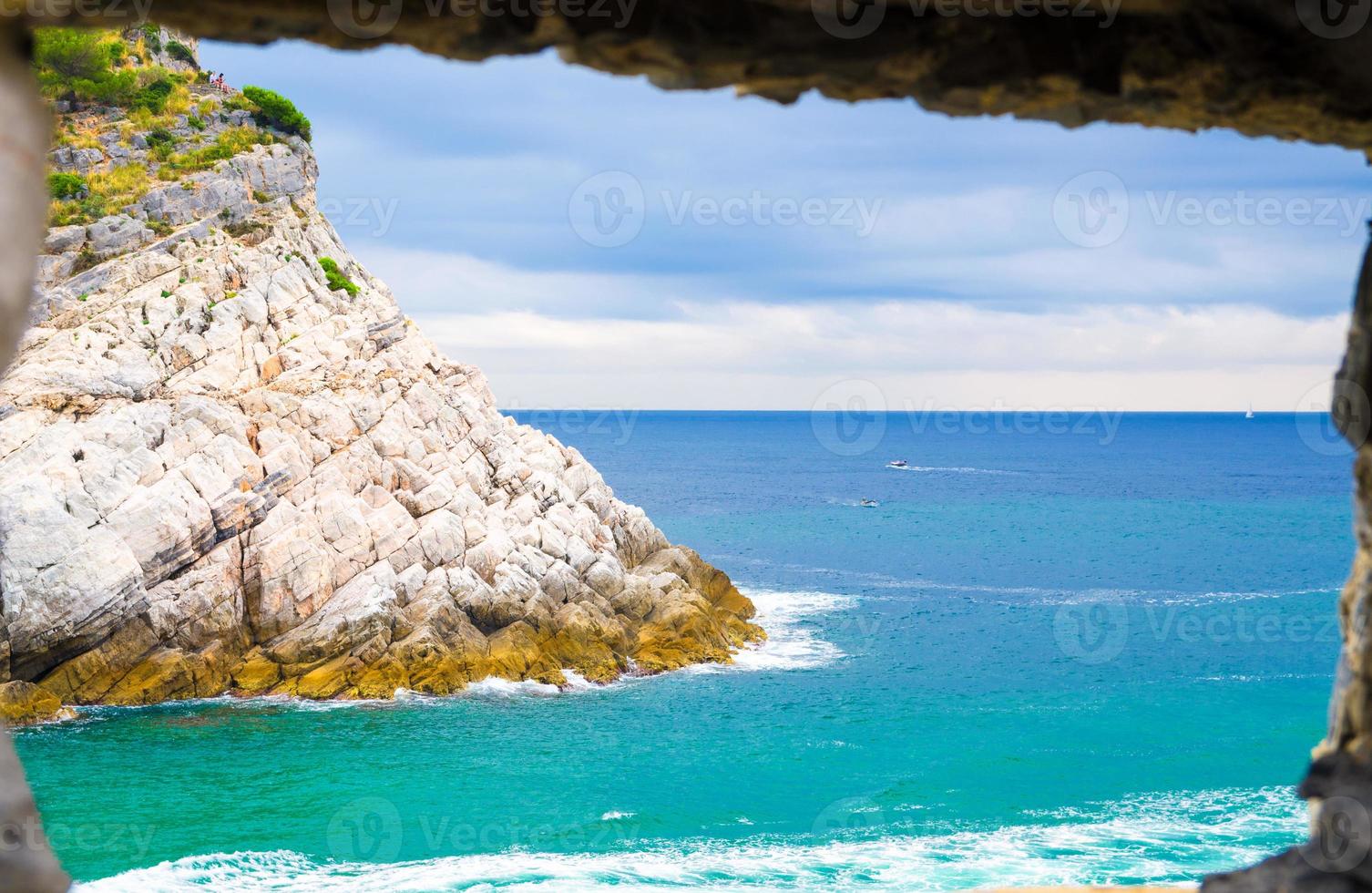 View of Ligurian sea water and rock cliff of Palmaria island through brick stone wall window of Portovenere coastal town photo