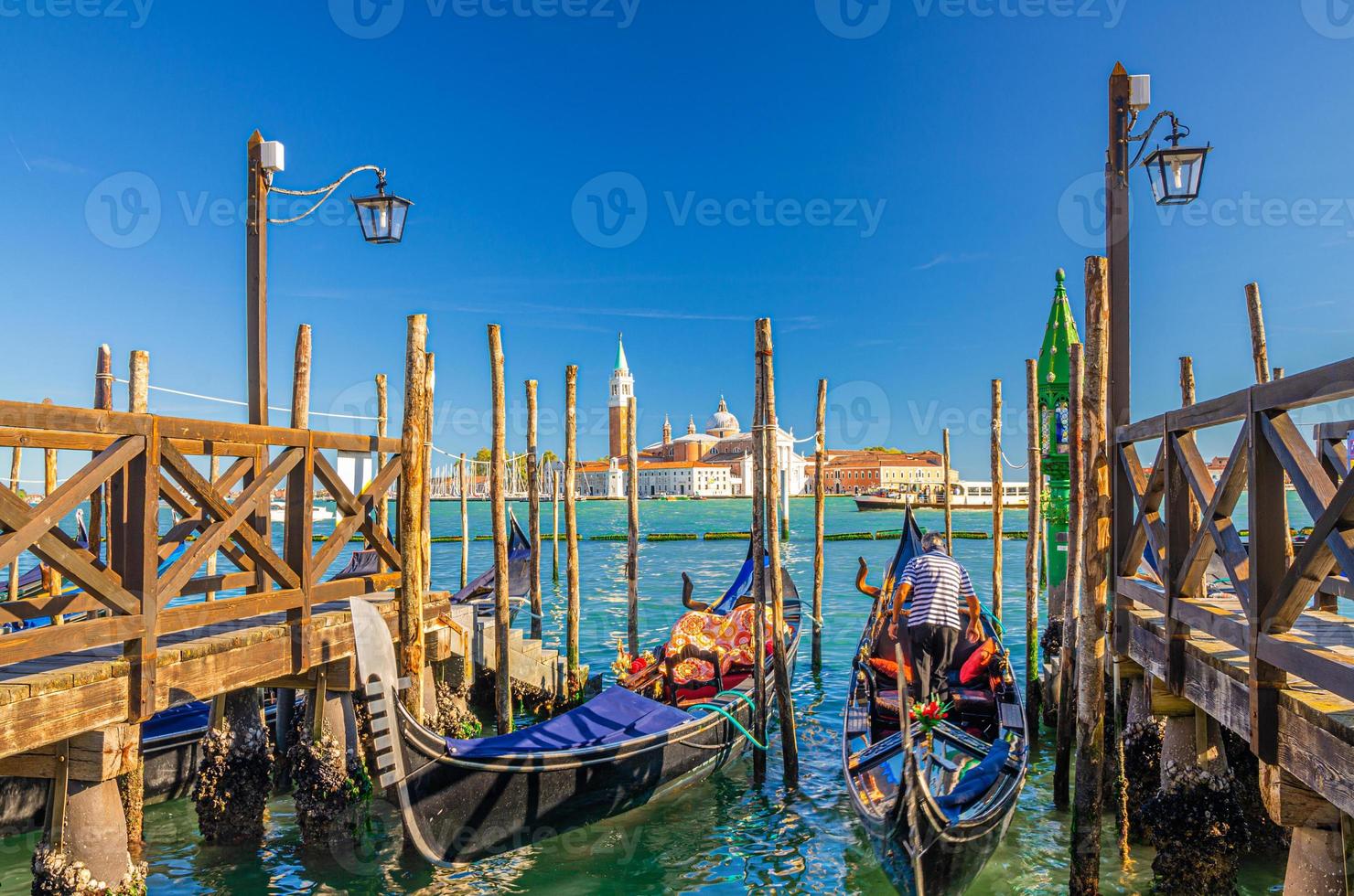 Gondolas moored docked at wooden pier in water of San Marco basin photo