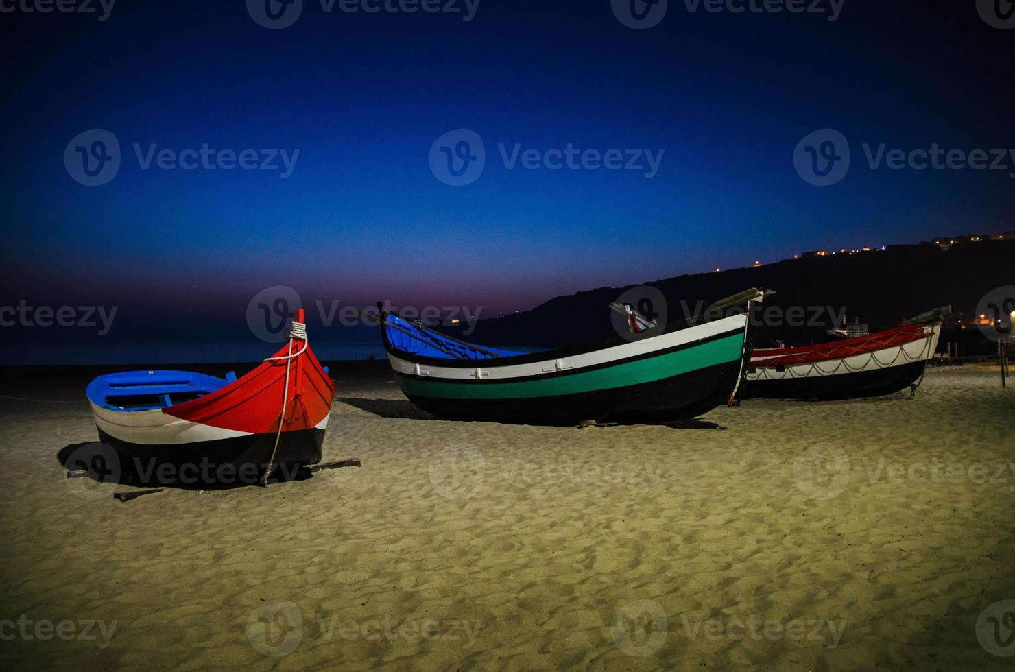 portugal, playa de nazare, barcos de madera de colores en la playa por la noche, vista panorámica de la ciudad de nazare foto