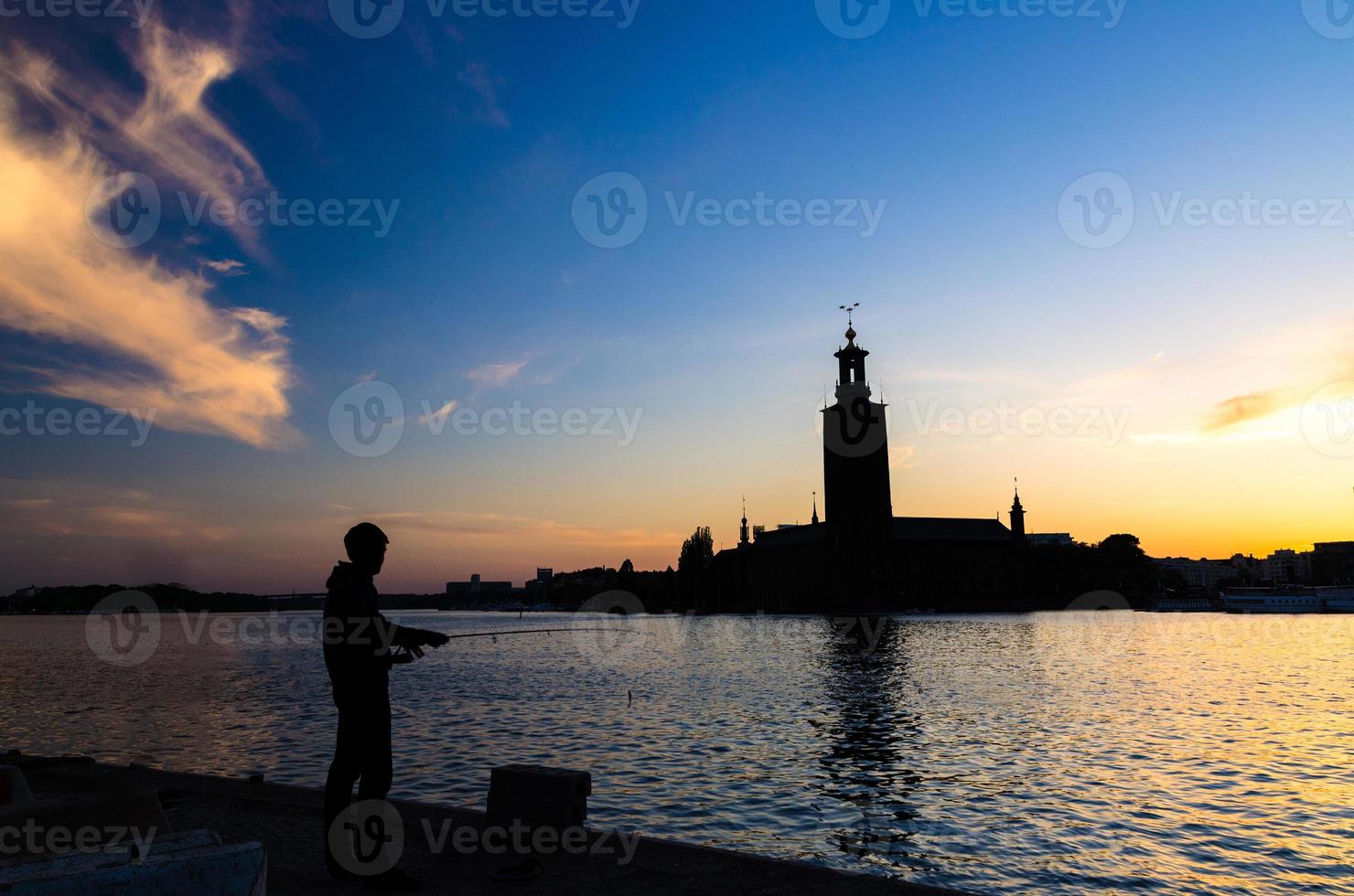 Silhouette of fisherman with pole and Stockholm City Hall, Sweden photo