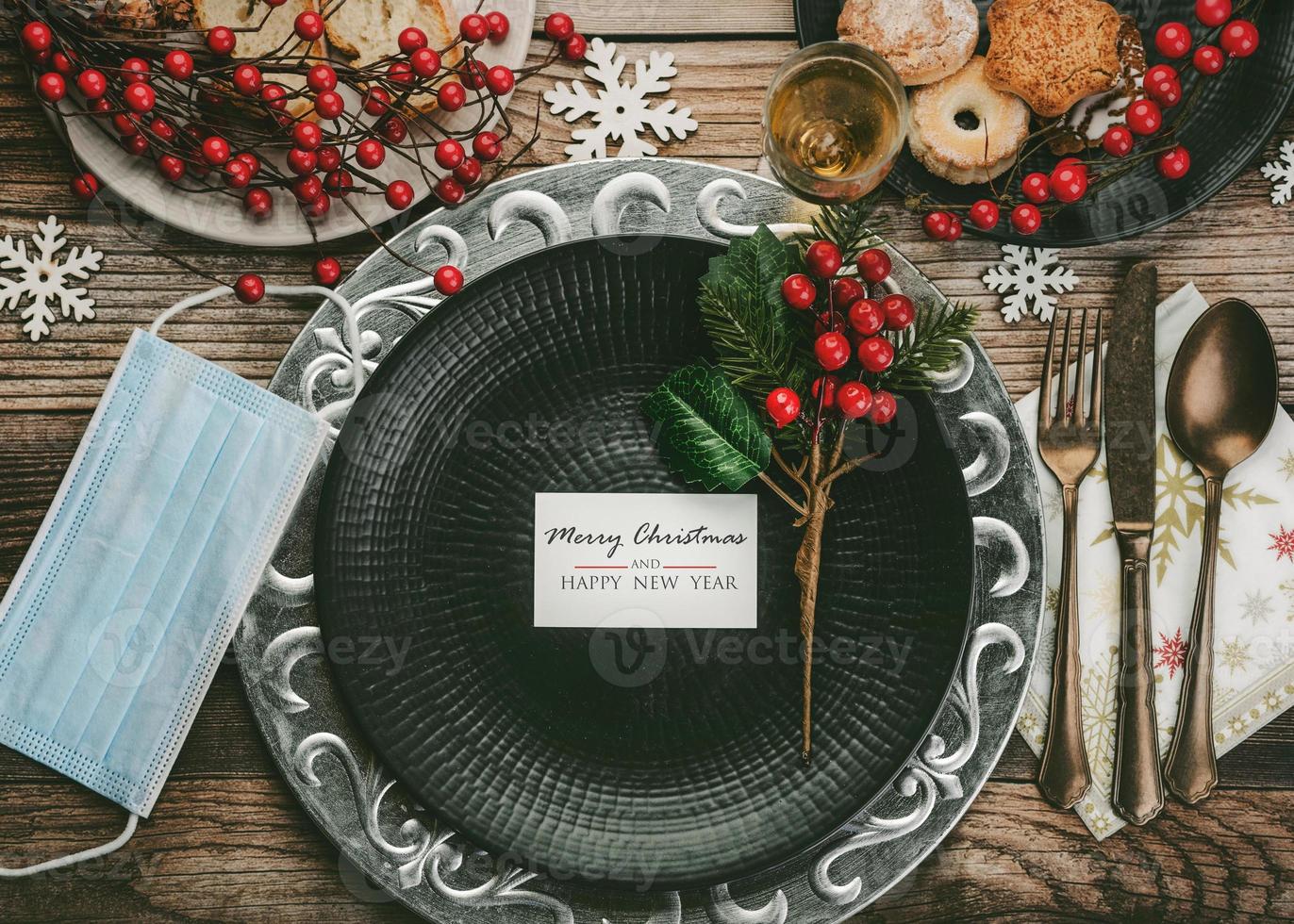 fondo del concepto de navidad cena de navidad con máscara médica, cubiertos antiguos vintage y diferentes platos de comida en la mesa de madera foto