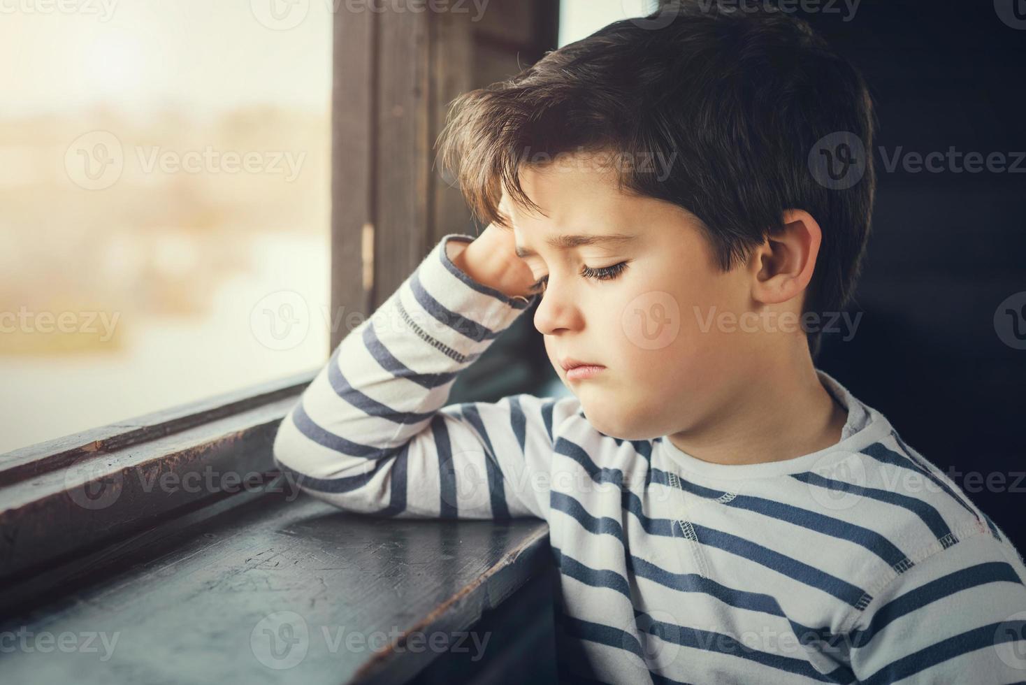 Sad boy next to a window photo