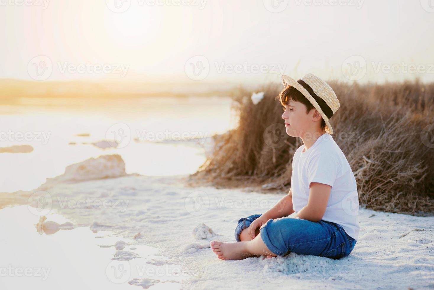 sad and pensive boy sitting on the beach photo