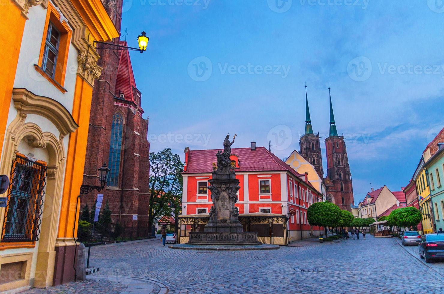 Monument on square, cobblestone road street with green trees, Cathedral of St. John the Baptist photo