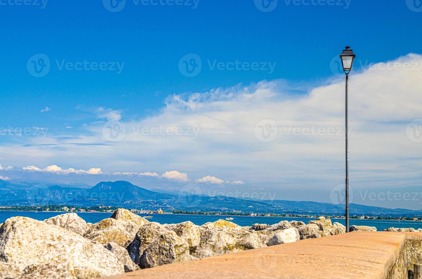 vista desde el muelle de piedra topo del agua del lago de garda con la cordillera de monte baldo y la península de sirmione foto