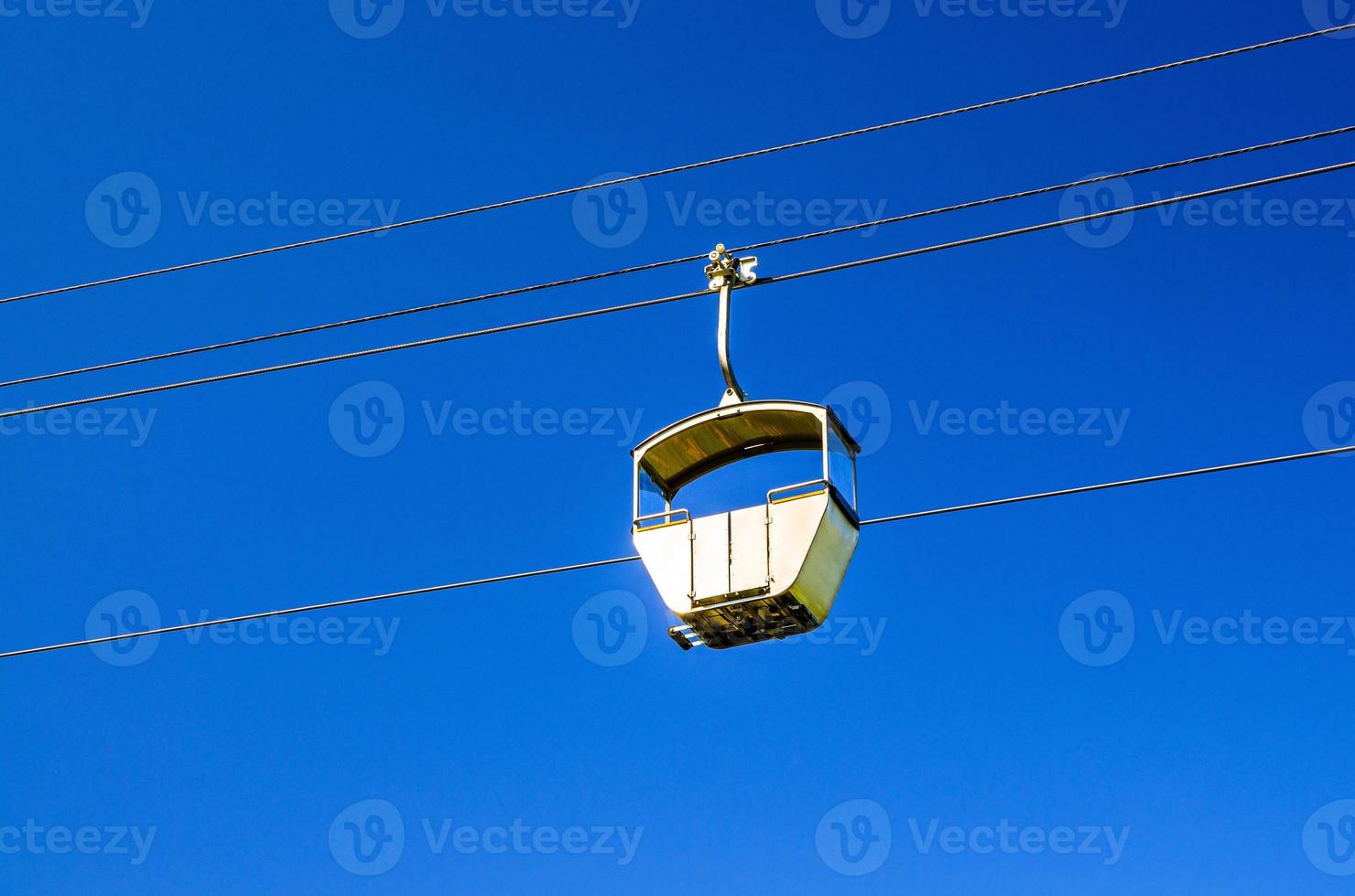 Cable car on rope of cableway, blue clear sky background in sunny summer day photo