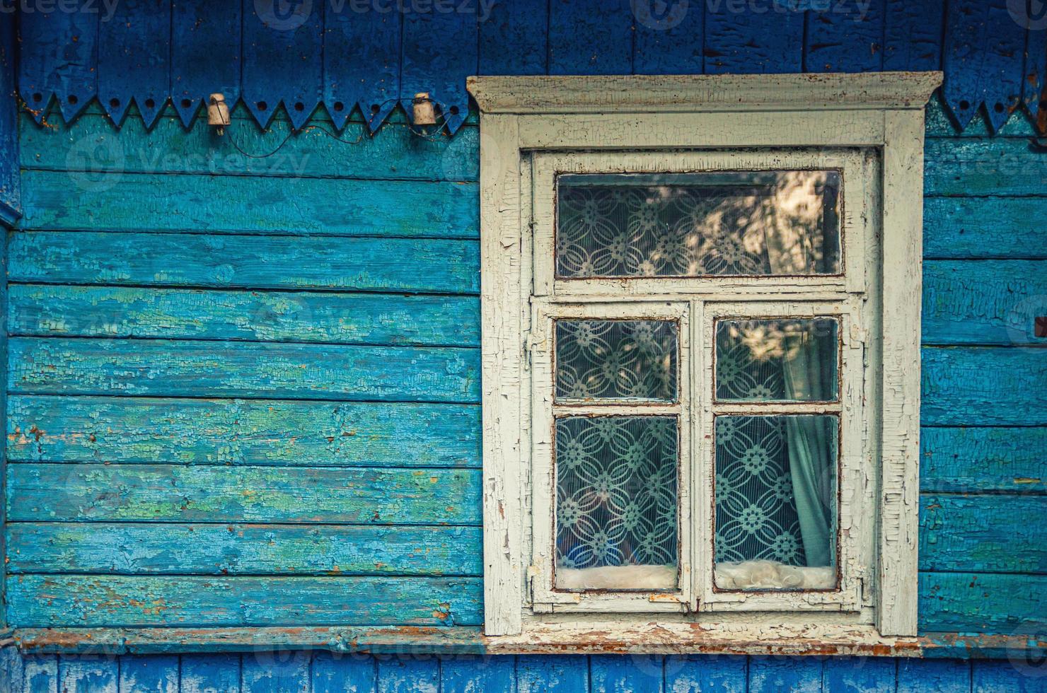 Shabby wooden wall and window with tulle of blue colored old house in village photo