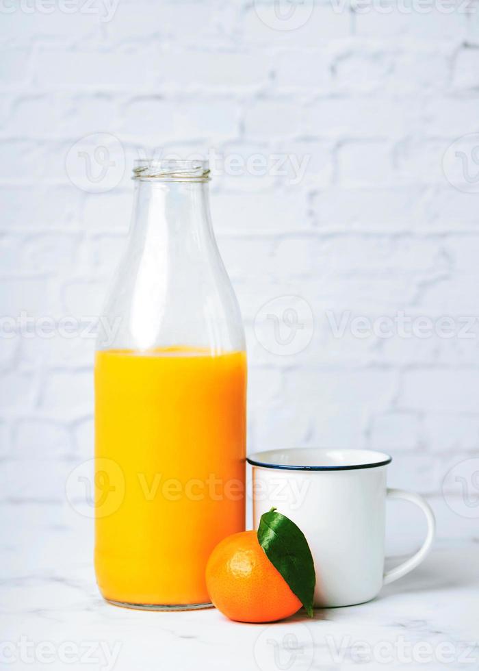 Fresh healthy orange juice in a glass bottle and tangerine next to a white cup photo