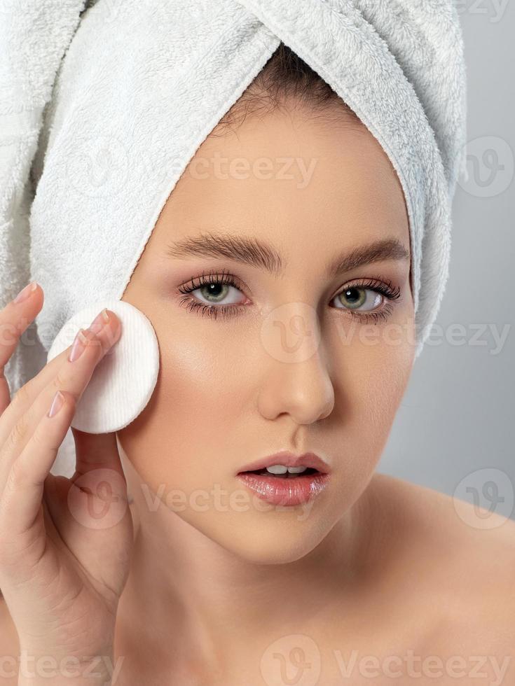 mujer joven limpiándose la cara con una almohadilla de algodón foto