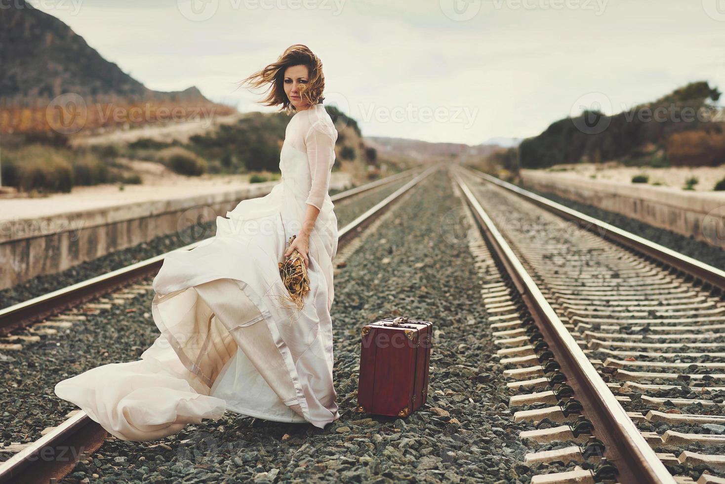 Pensive bride with a red suitcase on the train tracks photo